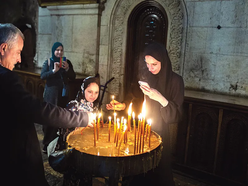 Palestinienii musulmani Mohammad Musa (stânga), Dareen Layla (spate), Lubna Musa (centru) și Eleen Musa (dreapta) aprind lumânări în interior biserica Sfântul Mormânt din Ierusalim (15 aprilie 2022) 