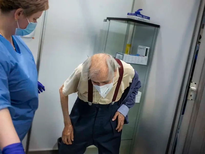 Petre Negut (91) undresses to receive the Pfizer-BioNTech COVID-19 vaccine at Romexpo in Bucharest, Romania, Friday, February. 12, 2021 Photo: Mugur VARZARIU/Getty Images/Newsweek