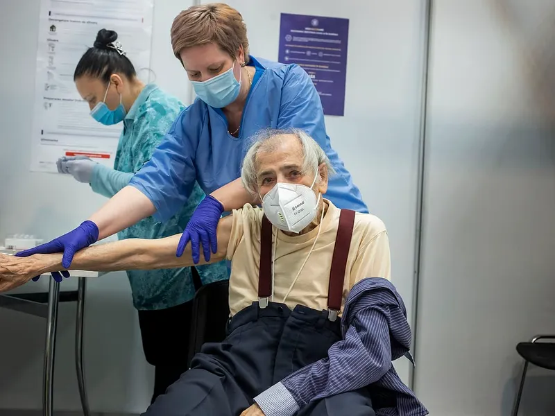 Petre Negut (91) undresses to receive the Pfizer-BioNTech COVID-19 vaccine at Romexpo in Bucharest, Romania, Friday, February. 12, 2021 Photo: Mugur VARZARIU/Getty Images/Newsweek.