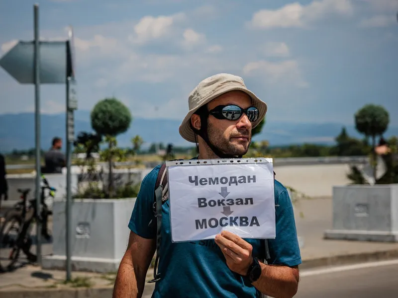 Un protestatar bulgar ține o pancartă, în timp ce personalul misiunii diplomatice a Rusiei și familiile lor sosesc pe aeroportul din Sofia - Foto: Profimedia Images